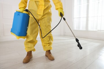 Fototapeta premium Pest control worker in protective suit spraying insecticide indoors, closeup