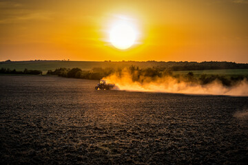 Tractor plows or sows the agricultural field at sunset
