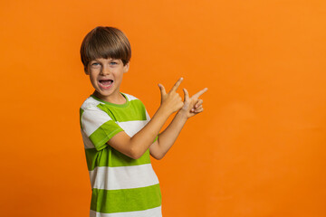 Preteen child boy kid showing thumbs up pointing right empty place, advertising area for commercial discount text, copy space for goods promotion advertisement. Little children on orange background