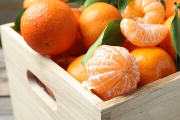 Fresh ripe tangerines with leaves in crate on table, closeup