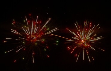 Bright red, yellow and green fireworks exploding against a dark night sky, sending sparks and streaks of light in multiple directions.