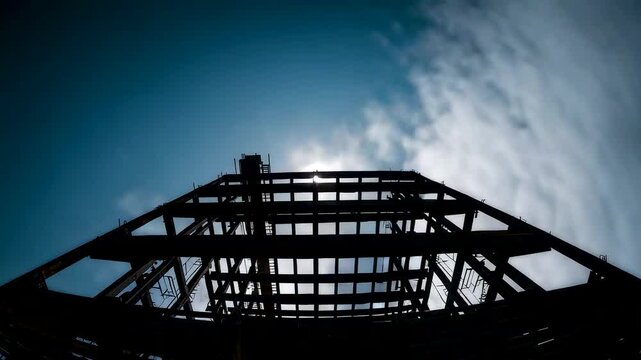 Low angle view of steel bridge framework silhouetted against dramatic sky, showing strong industrial structure, symmetry and open engineering design