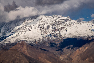 Dramatic snow-covered peaks of the Mustang Himal rising above the arid landscape of the Kali Gandaki Valley, photographed on the trekking route from Muktinath to Kagbeni in the Nepalese Himalayas. 
