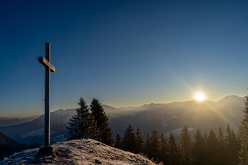 mountain summit cross in winter towards sunrise above the summits of Bregenzerwald in Vorarlberg Austria on a clear frosty morning 