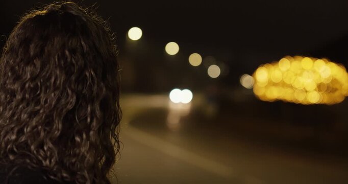 Cinematic slow-motion shot of a woman alone on a night street, turning her head to watch a car approach and drive past. Concept for loneliness, waiting, missed connection, and emotional.