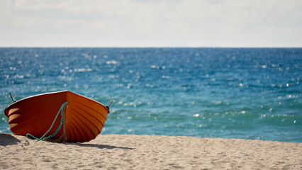 A small orange boat on a wide sandy beach with calm blue sea and large copy space, perfect for banners and travel promotions.