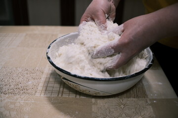 Hands mixing dough in a bowl on a kitchen table, homemade baking process with flour and grated ingredients, close-up food preparation scene showing rustic home cooking and traditional cuisine.