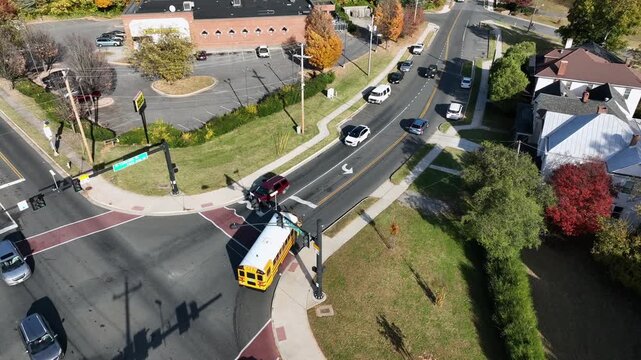 Aerial tracking shot of yellow school bus arriving at suburban school intersection in United States, with autumn foliage, cars and clear sunlight. Traffic scene on junction in U.S.