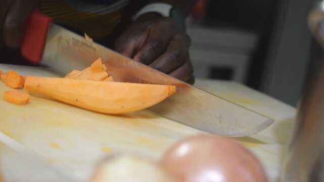 Professional chef uses a stainless steel knife to dice peeled orange-fleshed yams into a uniform concass&eacute; on a high-density white cutting board.