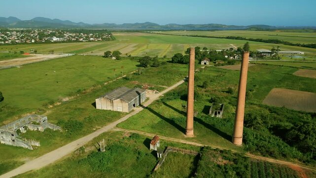 Cinematic drone shot: rising pull-away from an abandoned sugar and alcohol mill in Sampaio Correa. Historic chimneys and ruins surrounded by green rural landscape in Saquarema, Rio de Janeiro. 4K.