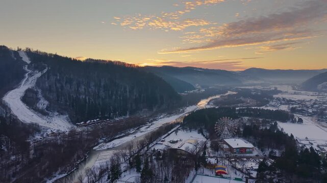 Video of Gura Humorului city in Romania at sunset showing snowy P&acirc;rtia Șoimul ski slope on hill, Moldova River in valley, and Ferris wheel in Arinis Park area