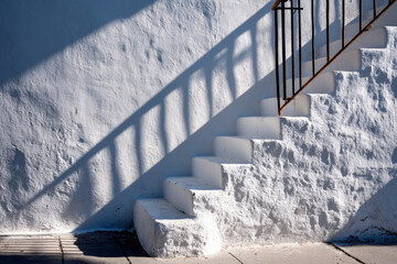 Sunlit minimalist alley with white plaster pedestal and fire escape shadow pattern