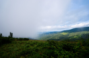 A scenic view of a lush green valley surrounded by forested hills under a partly cloudy sky.