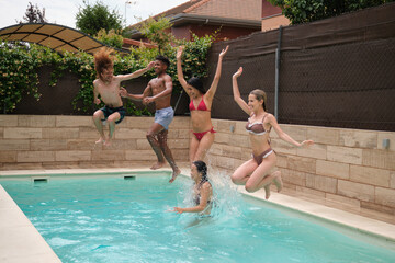 Five young adults jumping into a swimming pool in a backyard during summer holidays