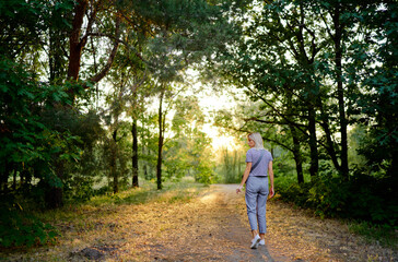 Obraz premium Woman Walking Along Forest Path During Sunset in Summer