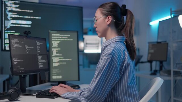 Asian female software engineer developing coding on multiple monitors in office. Woman programmer writing scripts and developing software on computer, cyber security and programming concept.