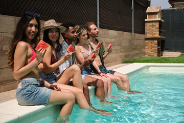 Group of young happy multi ethnic friends enjoying watermelon by the pool during summer holidays
