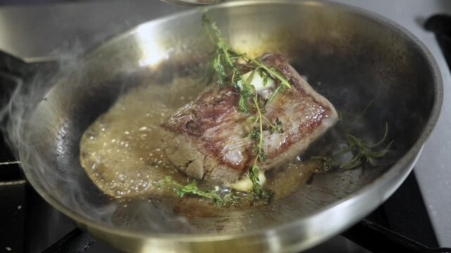 Experienced chef basting a seared filet mignon with butter, garlic and herbs in a sizzling steel pan, creating a juicy, aromatic gourmet steak ready to serve
