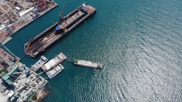 Dry dock vessel and several bulk carriers stay at berth, industrial shore at Tsing Yi island. Cement factory supply ships or barges. Aerial top view shot
