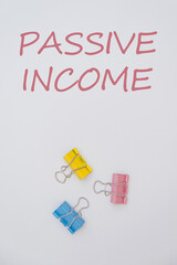 Colorful paper clips in yellow, blue, and pink arranged on a white background with the text 'Passive Income' written above.