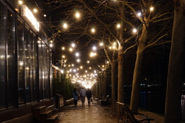 Path along Dambovita river with cafes on the left, illuminated with yellow lights for Christmas in Bucharest, Romania at night
