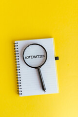 A magnifying glass is placed over a notebook with the word 'MOTIVATION' written on a yellow background. The scene emphasizes focus and inspiration.