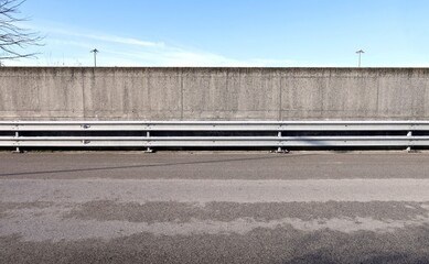 Metalllic crash barrier next to a rough surrounding concrete wall. Sky above and road in front. Background for copy space
