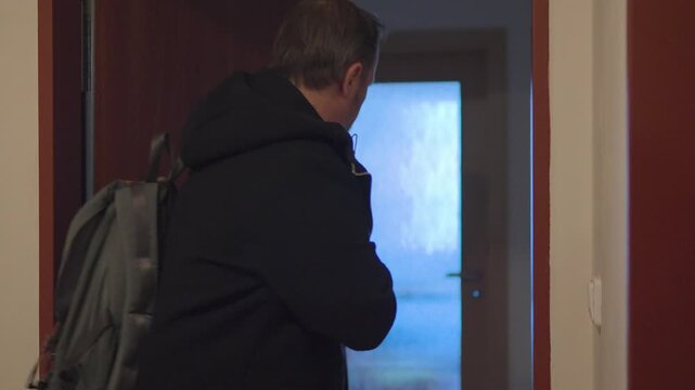 A handsome middle-aged man walks out of his apartment and closes the door behind him