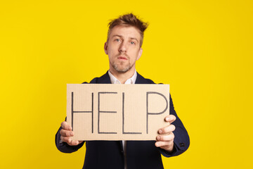 Unhappy businessman holding cardboard sign with word Help on yellow background