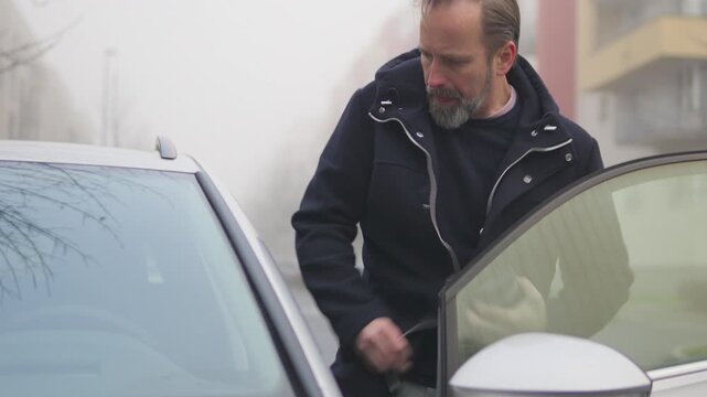 A handsome middle-aged man gets into a car in a suburban area