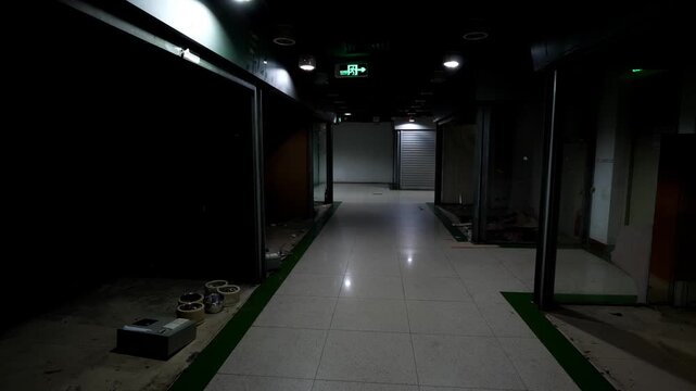 Dark rooms at former shopping mall, open sections immersed in shadow, abandoned commercial center at Chinese city, dim light. POV camera look to scary empty place, stay in illuminated passage.