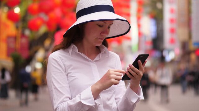 Tourist woman stay and stare to phone, blurred background. Lady using smartphone at Beijing Lu pedestrian street, popular shopping district at Guangzhou city