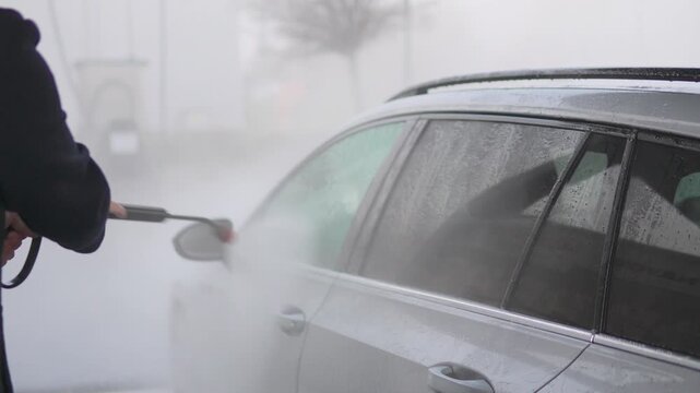 A middle-aged Caucasian man power washes the side, top, and wheel of his car