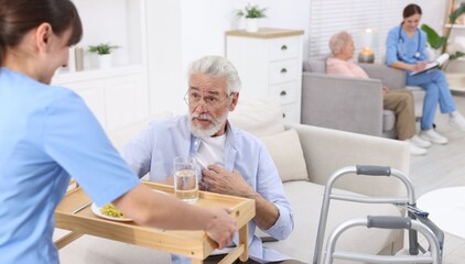 Obraz premium Care worker serving dinner to senior man at retirement home