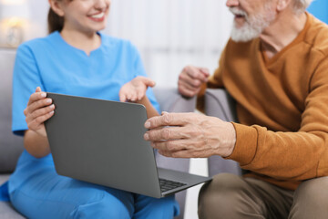 Obraz premium Care worker teaching senior man to use laptop at retirement home, closeup
