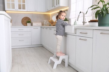 Child safety at home. Little girl climbing to open tap at sink in kitchen