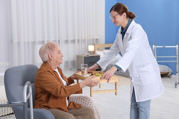 Care worker serving dinner to senior woman at retirement home