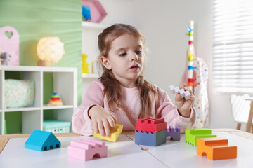 Little girl playing with toys at white table in playroom