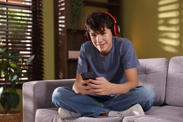 Obraz premium Teenage boy in headphones with smartphone on sofa at home