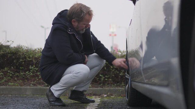 A handsome middle-aged man wipes the hubcap on a front wheel of his car