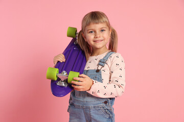 Portrait of smiling little girl with penny board on pink background