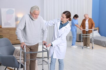 Fototapeta premium Care workers helping man and woman with walkers at retirement home, selective focus