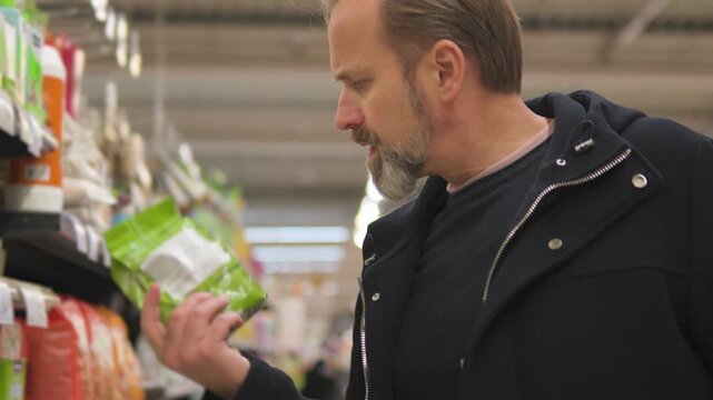 A handsome middle-aged man picks pet food in a supermarket - closeup