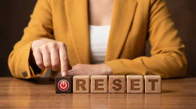 Woman in yellow suit pushing power button with wooden blocks for life reset concept looking serious on decision to start new business or career