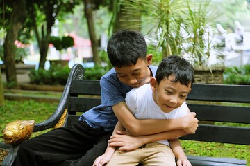 Two brothers sharing a warm hug while sitting on a park bench, expressing love, protection,and emotional connection in a green outdoor environment.This candid family moment highlights mental wellbeing