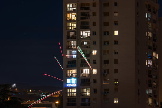 Long exposure fireworks trails captured near a tall apartment building in Rijeka, creating dynamic light lines against the dark night sky - Powered by Adobe