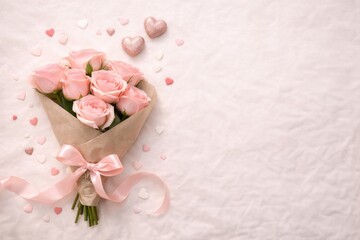 Minimalist and romantic flat lay composition; a beautiful bouquet of fresh pink roses wrapped in brown craft paper with a silk pink ribbon bow. Surrounded by small pastel and glittery heart decoration
