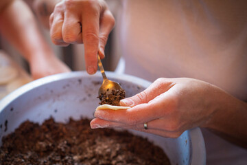 A pair of hands carefully scoops flavorful filling onto a delicate dough circle, preparing handmade dumplings