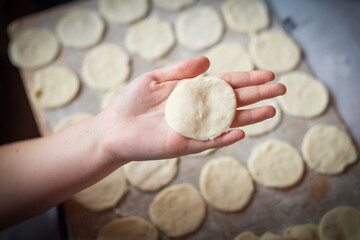 A hand holds a perfectly formed round of dough, surrounded by numerous similar dough pieces on a wooden surface