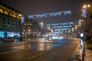 Wide city avenue at night decorated with elegant holiday light arches over roadway creating festive urban winter atmosphere with traffic glow